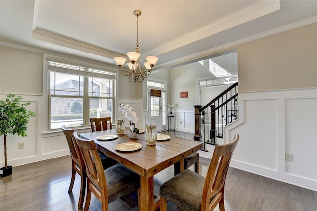 dining space with a tray ceiling, a healthy amount of sunlight, a chandelier, and a decorative wall