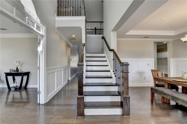 staircase with a towering ceiling, wood finished floors, ornamental molding, and a decorative wall