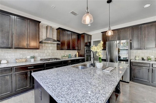 kitchen featuring ornamental molding, decorative backsplash, stainless steel appliances, wall chimney exhaust hood, and a sink