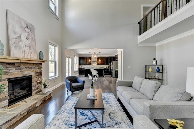 living area featuring dark wood-style floors, baseboards, a high ceiling, ornamental molding, and a stone fireplace