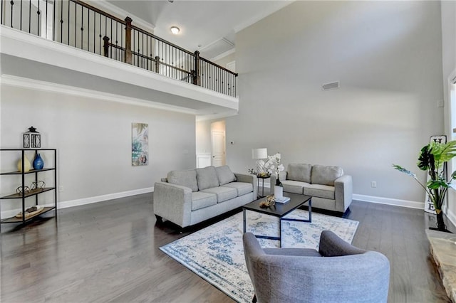 living room featuring wood finished floors, visible vents, baseboards, a towering ceiling, and crown molding