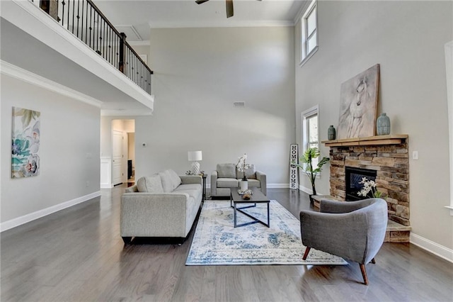 living room with wood finished floors, baseboards, a ceiling fan, a fireplace, and crown molding