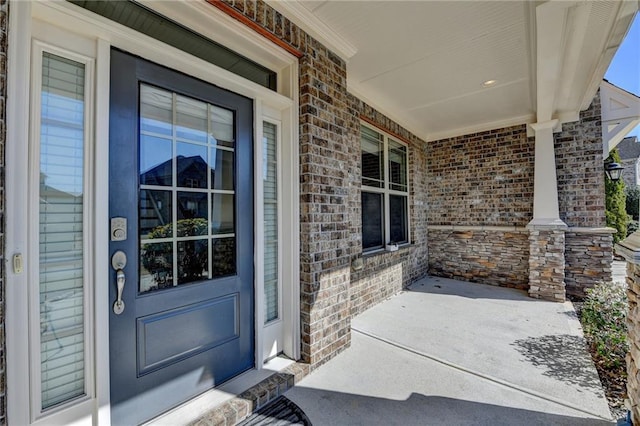 view of exterior entry with brick siding and a porch