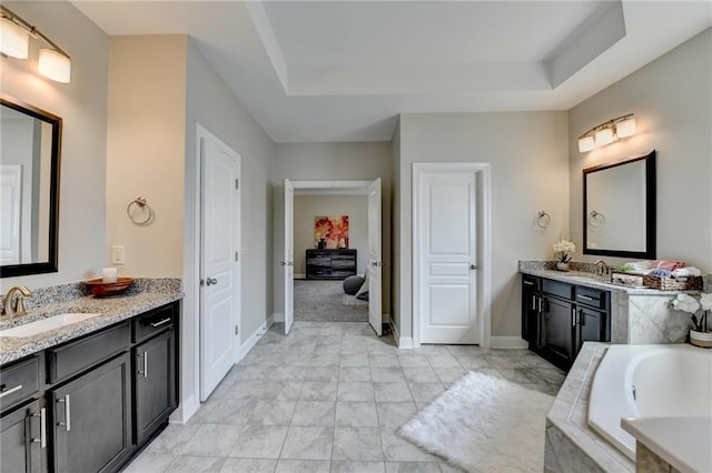 bathroom featuring a raised ceiling, two vanities, tiled tub, and a sink