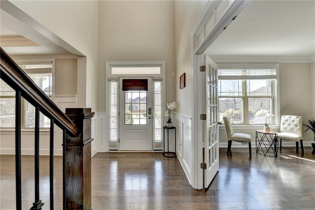 entrance foyer with dark wood finished floors, a decorative wall, stairs, and ornamental molding