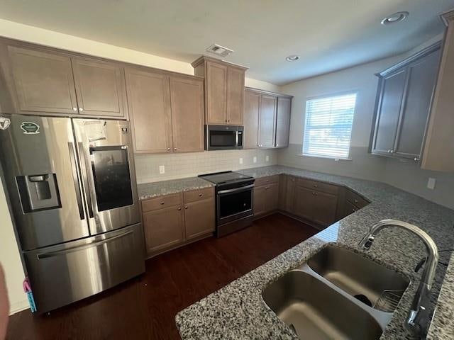 kitchen featuring sink, dark hardwood / wood-style floors, decorative backsplash, light stone countertops, and appliances with stainless steel finishes