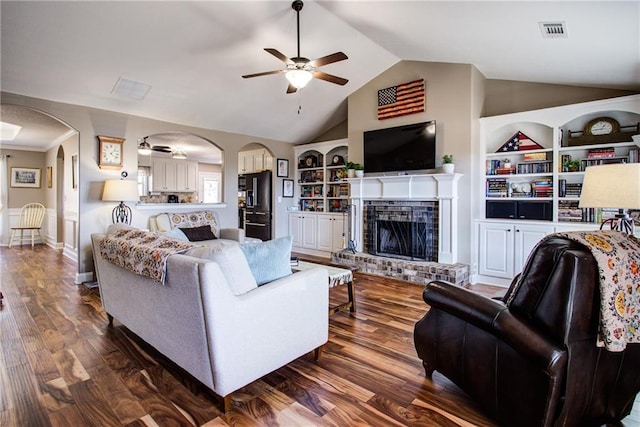 living room with built in shelves, lofted ceiling, a brick fireplace, dark hardwood / wood-style floors, and ceiling fan