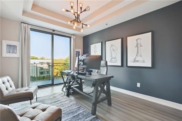 office area featuring a notable chandelier, a raised ceiling, and hardwood / wood-style floors