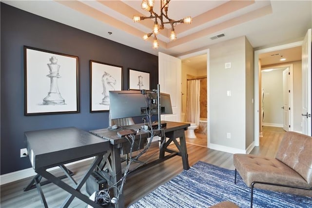 home office with a notable chandelier, a raised ceiling, and wood-type flooring