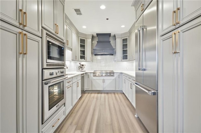 kitchen with built in appliances, tasteful backsplash, custom exhaust hood, and light hardwood / wood-style floors