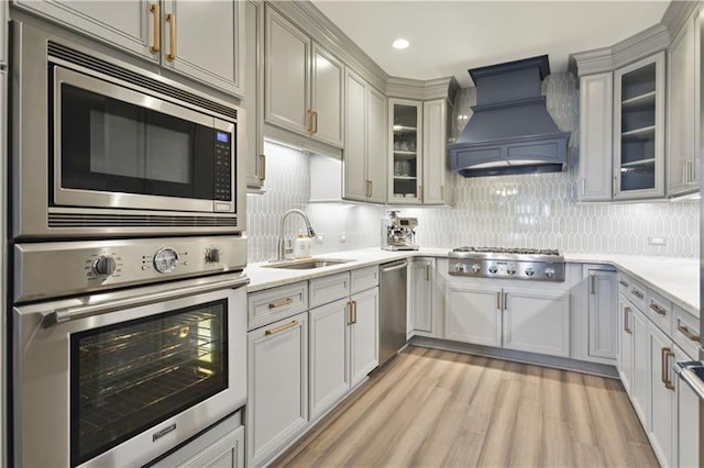 kitchen with light wood-type flooring, stainless steel appliances, backsplash, sink, and custom exhaust hood