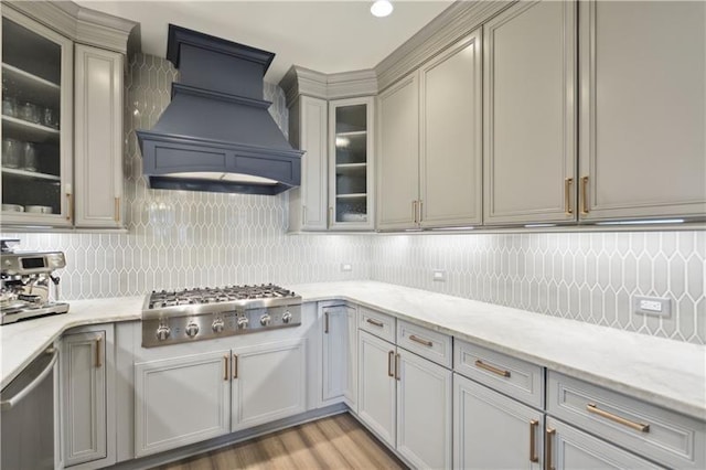 kitchen featuring decorative backsplash, light stone counters, stainless steel appliances, and custom range hood