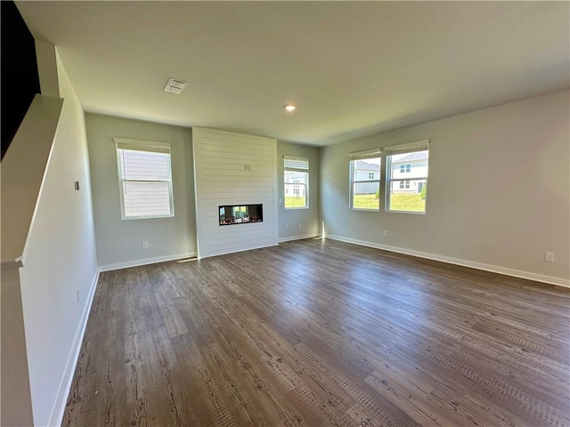 unfurnished living room with a large fireplace, dark wood-style floors, visible vents, and baseboards