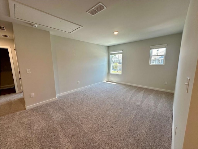 carpeted spare room with attic access, visible vents, and baseboards