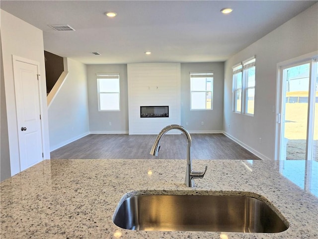 kitchen with light stone counters, a sink, visible vents, open floor plan, and a glass covered fireplace