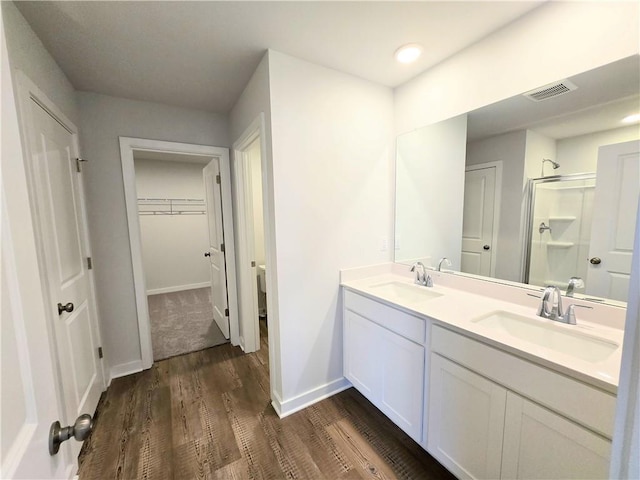 bathroom featuring wood finished floors, a sink, visible vents, and a shower stall