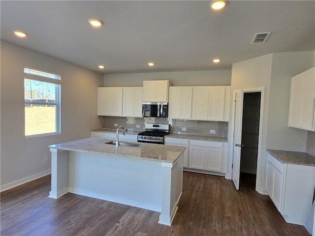 kitchen with visible vents, backsplash, appliances with stainless steel finishes, a sink, and an island with sink