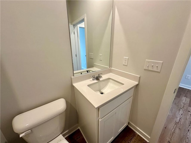 half bath with toilet, baseboards, and vanity