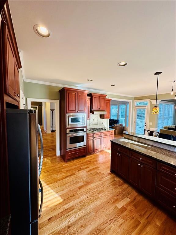 kitchen with pendant lighting, appliances with stainless steel finishes, ornamental molding, and light hardwood / wood-style flooring