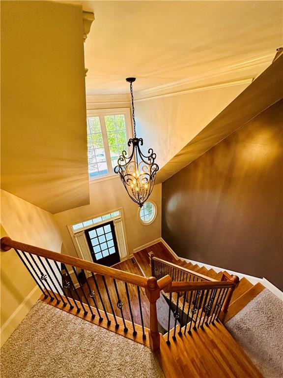 staircase with crown molding and an inviting chandelier