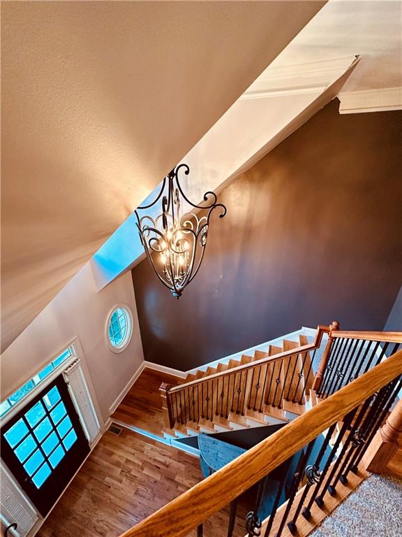 staircase with vaulted ceiling, a notable chandelier, and hardwood / wood-style floors