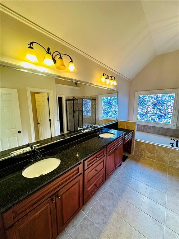 bathroom with tiled tub, vaulted ceiling, tile patterned floors, and vanity