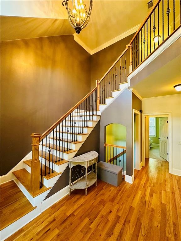 stairs featuring ornamental molding, high vaulted ceiling, a notable chandelier, and hardwood / wood-style floors