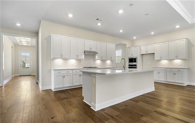 kitchen with white cabinets, a center island with sink, and built in microwave