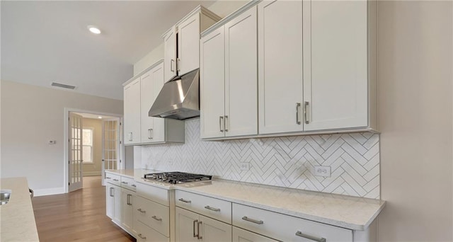 kitchen with tasteful backsplash, light stone countertops, light hardwood / wood-style flooring, and white cabinets