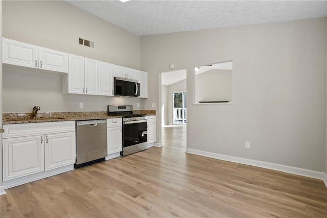 kitchen featuring visible vents, stone counters, lofted ceiling, a sink, and appliances with stainless steel finishes