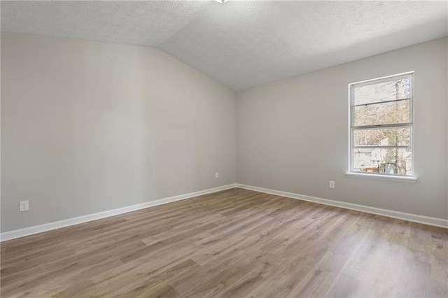 empty room featuring light wood-type flooring, lofted ceiling, a textured ceiling, and baseboards