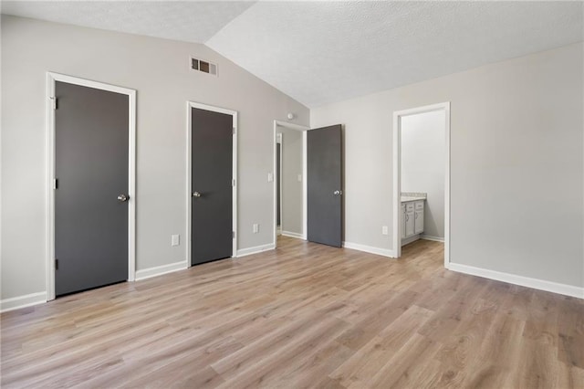 unfurnished bedroom featuring light wood finished floors, visible vents, a textured ceiling, and vaulted ceiling