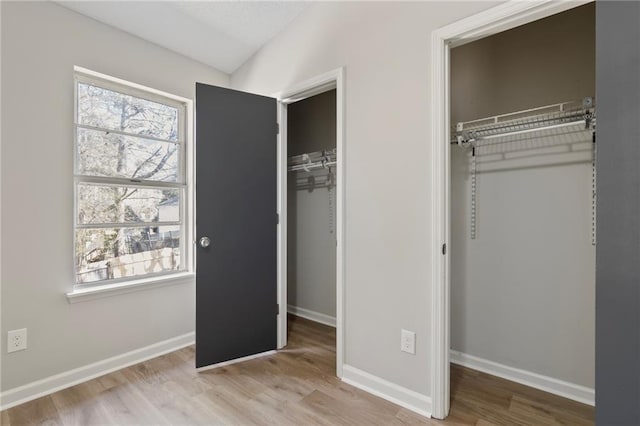 unfurnished bedroom featuring baseboards, wood finished floors, multiple closets, and vaulted ceiling