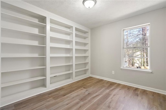 spare room featuring built in shelves, baseboards, a textured ceiling, and wood finished floors