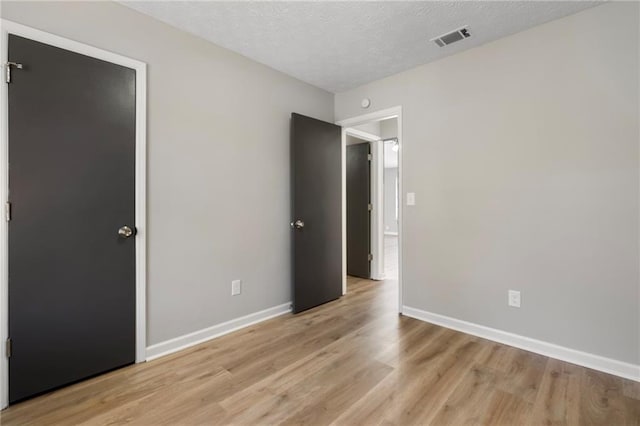 unfurnished bedroom with baseboards, visible vents, a textured ceiling, and light wood-style floors