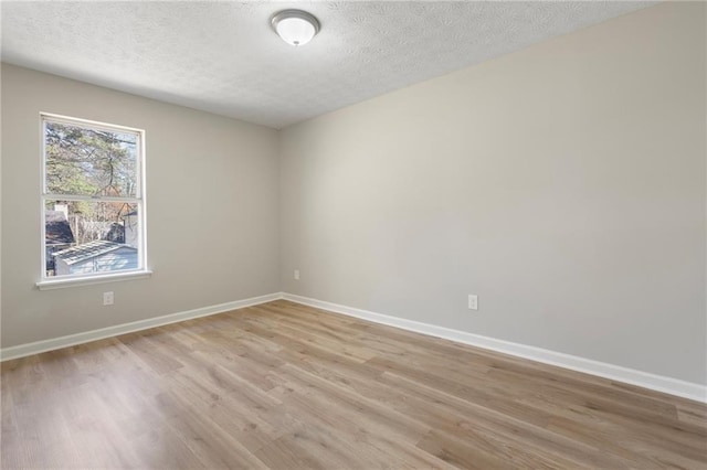 spare room with light wood finished floors, a textured ceiling, and baseboards