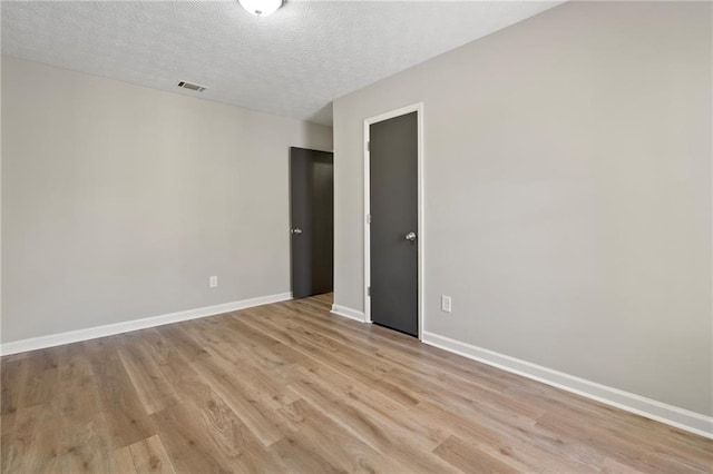 spare room featuring visible vents, baseboards, a textured ceiling, and light wood-style flooring