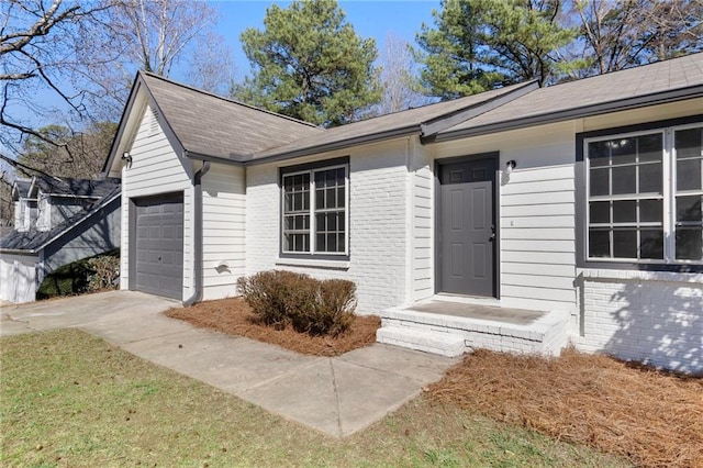 view of exterior entry with a garage, brick siding, and driveway