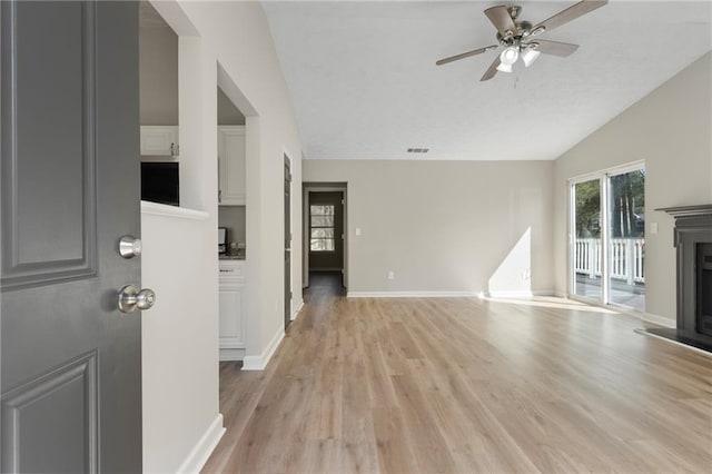 unfurnished living room featuring a ceiling fan, baseboards, light wood finished floors, lofted ceiling, and a fireplace with raised hearth