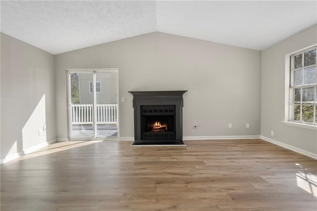 unfurnished living room featuring a textured ceiling, wood finished floors, a lit fireplace, baseboards, and vaulted ceiling