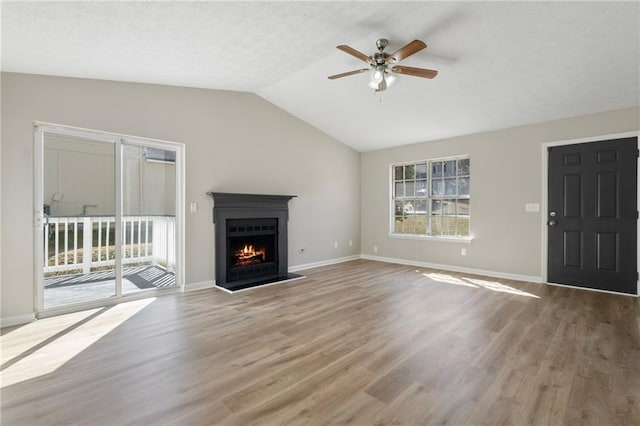 unfurnished living room featuring a lit fireplace, vaulted ceiling, wood finished floors, a textured ceiling, and a ceiling fan