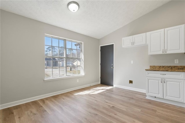 unfurnished dining area with a textured ceiling, light wood-type flooring, baseboards, and vaulted ceiling