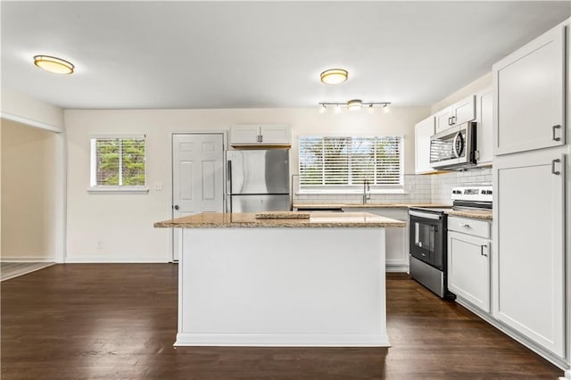 kitchen with light stone counters, a kitchen island, appliances with stainless steel finishes, backsplash, and dark wood finished floors