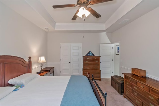 bedroom with light colored carpet, ceiling fan, a raised ceiling, crown molding, and a closet