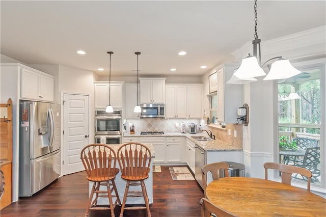 kitchen with appliances with stainless steel finishes, sink, white cabinets, and decorative light fixtures