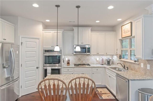 kitchen featuring sink, appliances with stainless steel finishes, light stone counters, white cabinets, and decorative light fixtures