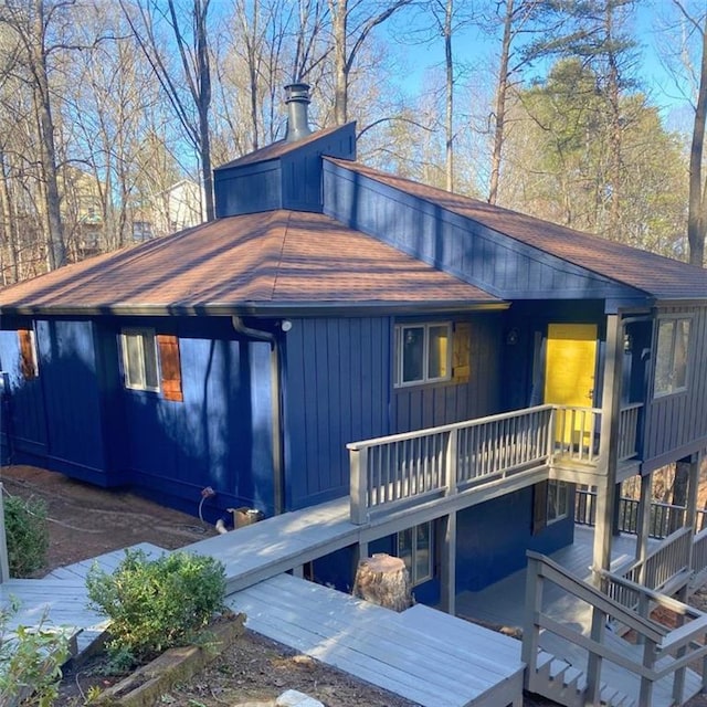 rear view of house featuring roof with shingles, board and batten siding, and a wooden deck