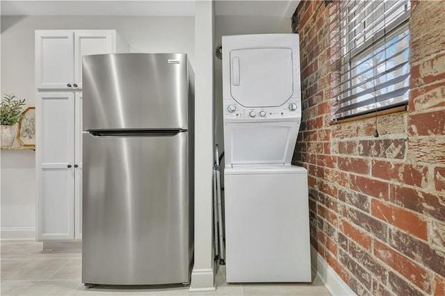 laundry area featuring stacked washer and dryer, light tile patterned flooring, and brick wall