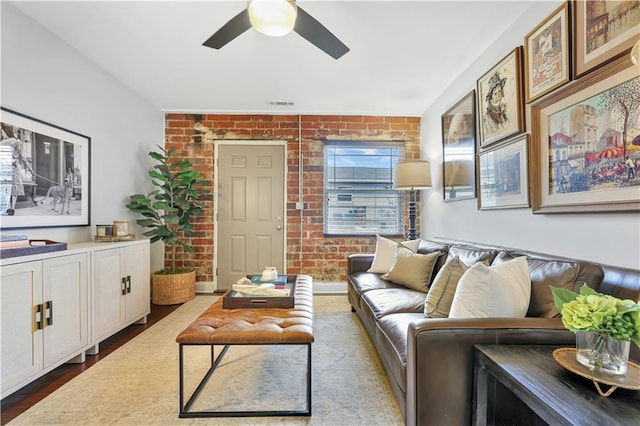 living room featuring wood-type flooring, brick wall, and ceiling fan