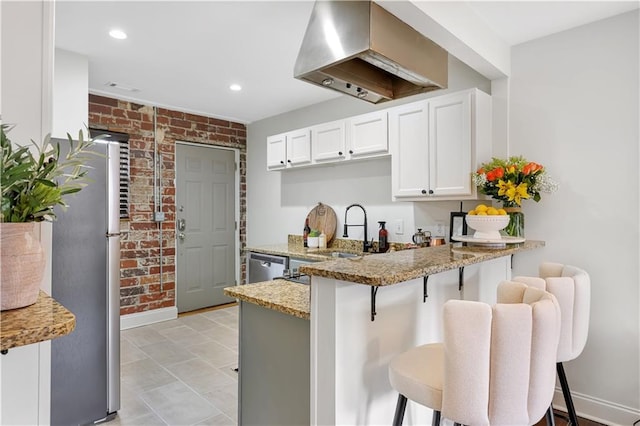 kitchen with a breakfast bar, light stone counters, appliances with stainless steel finishes, brick wall, and white cabinets